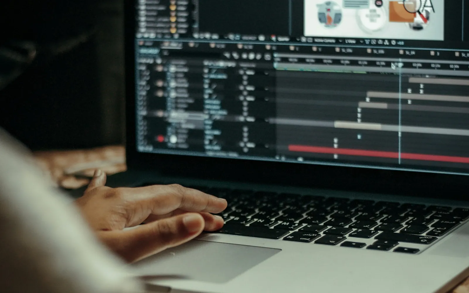 A motion designer building a layered animation timeline in compositing software on a laptop.