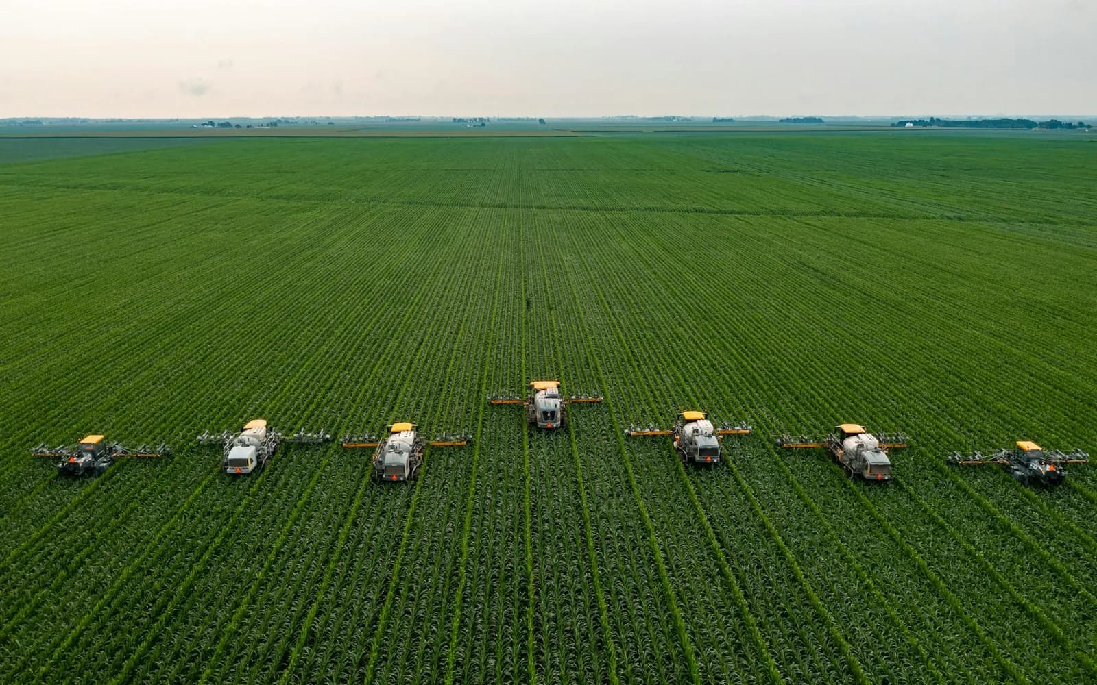 An aerial view of crop sprayers working in formation across a large field.