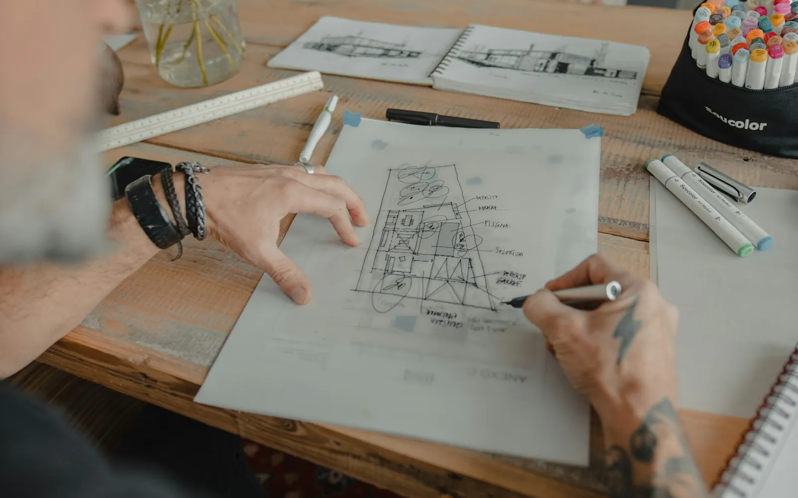An architect sketching a floor plan with pens and a scale ruler.