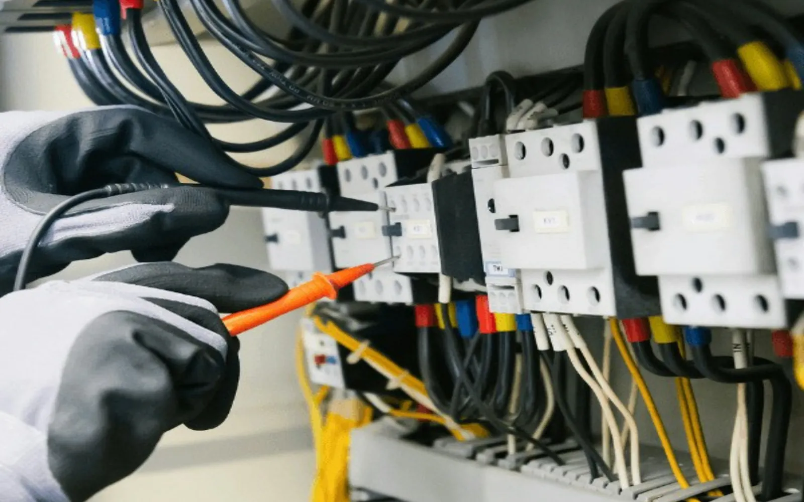 A technician testing an electrical distribution panel with a multimeter.