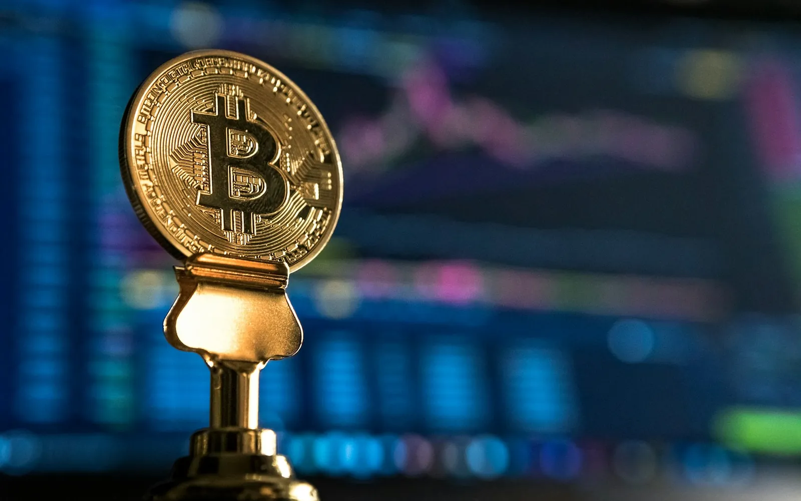A bitcoin coin in front of a screen of market data.
