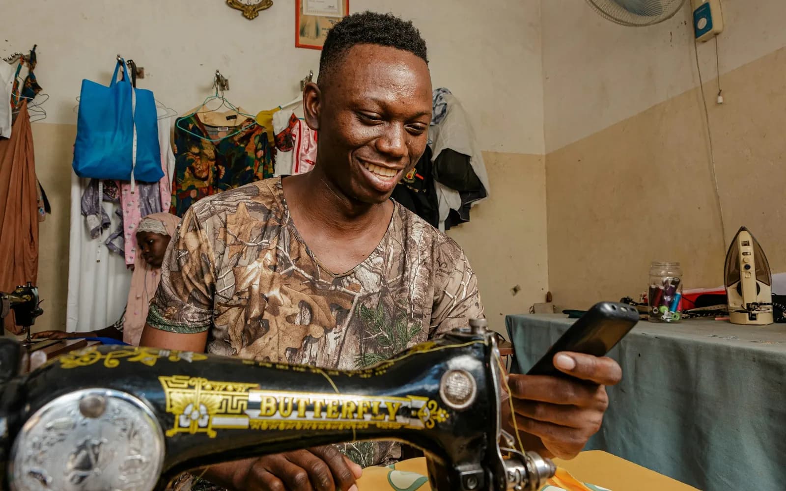 A tailor running his own business, smiling at his sewing machine.